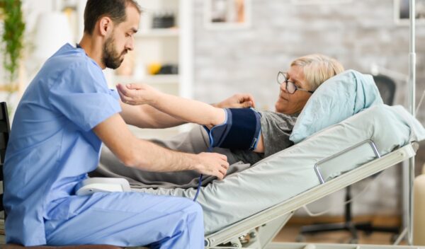 Young male doctor taking the blood pressure of senior woman in nursing home